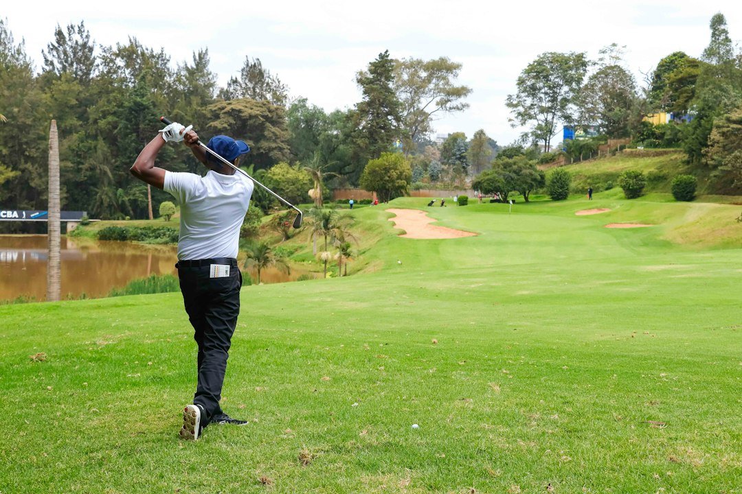 A golfer swinging a club on a lush green course with water and trees