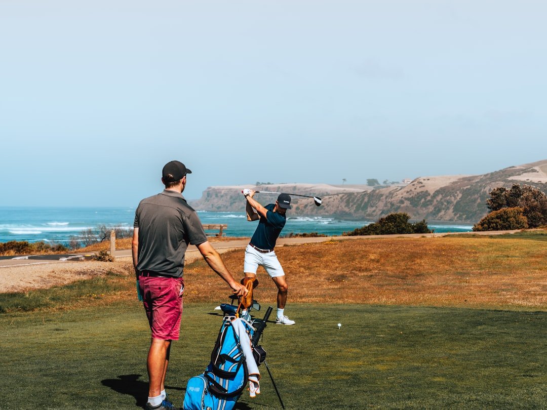 Two golfers standing near a tee box on a coastal golf course.